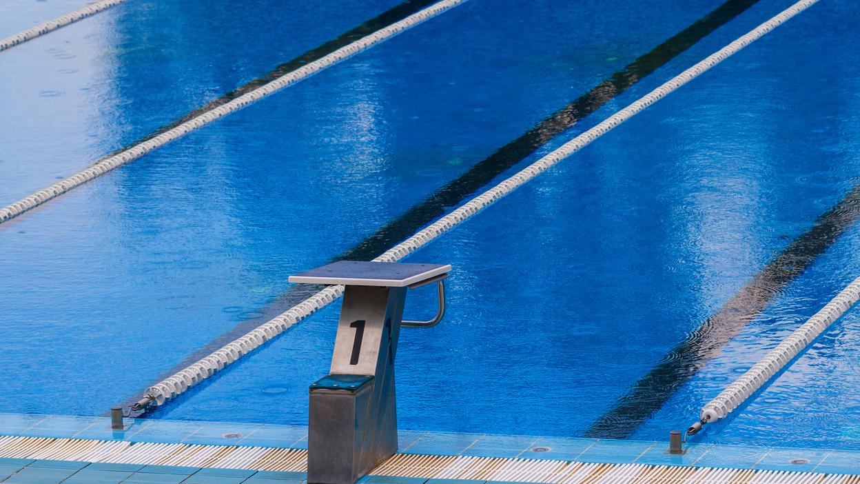 Startblock mit der Nummer 1 am Beckenrand eines Schwimmbeckens mit blauen Wasserbahnen im Hintergrund.