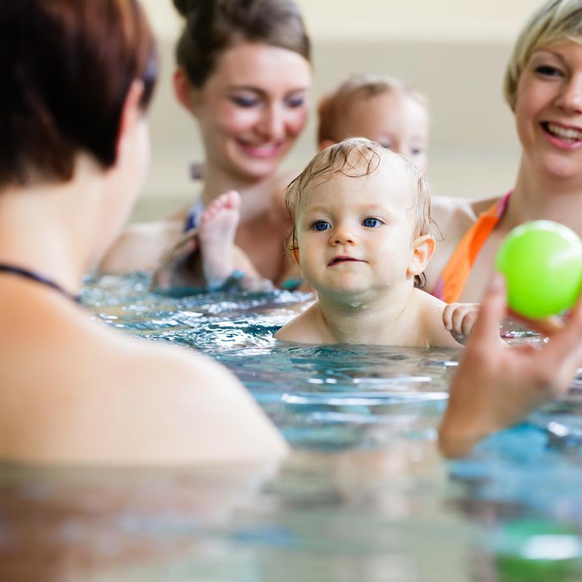 Gruppen von Frauen mit Kleinkindern im Wasser, während eines Spielens mit einem grünen Ball.
