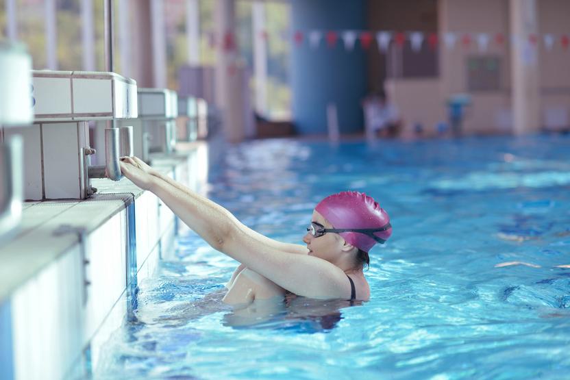 Schwimmerin mit rosa Badekappe und Schwimmbrille greift nach dem Beckenrand in einem Hallenbad.
