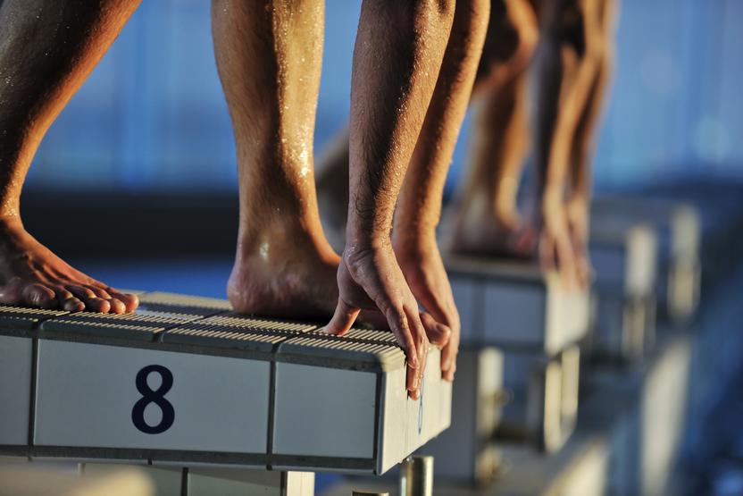 Nahaufnahme von Füßen und Händen von Schwimmern, die auf einem Startblock mit der Nummer 8 stehen.