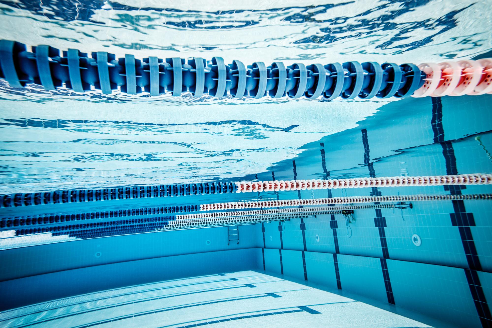 Unterwasseraufnahme eines Schwimmbeckens mit blauen und roten Schwimmbahnmarkierungen sowie klarer Wasseroberfläche.